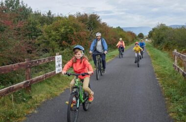 Family cycling on scenic path, enjoying nature near hotel, surrounded by lush greenery and mountain views.