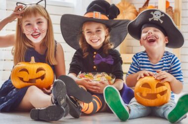 Children in Halloween costumes, smiling with carved pumpkins, in a bright hotel lobby, experiencing a festive stay.