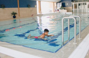 Child enjoying indoor heated pool with clear blue water and poolside plants at a welcoming family-friendly hotel.