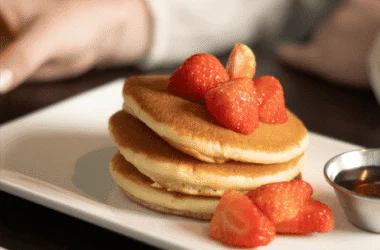 Stack of fluffy pancakes topped with fresh strawberries, served with syrup in a luxurious hotel dining setting.