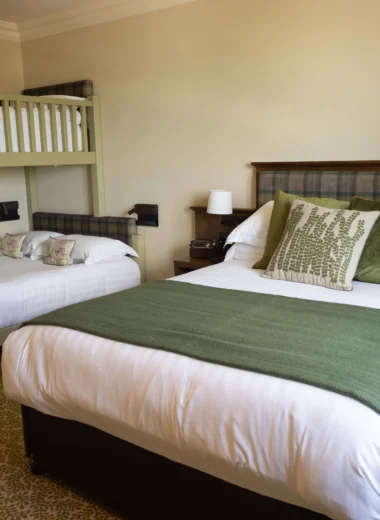Spacious family room with cosy double bed, stylish bunk beds, plush green accents, and warm lighting, ideal for relaxation.