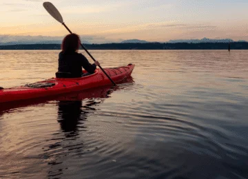 Person kayaking at sunset on tranquil lake with mountain views