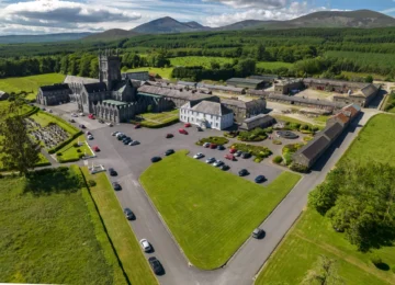 Aerial view of the historic architecture of mount mellery abbey, lush gardens, ample parking, and scenic mountain backdrop.