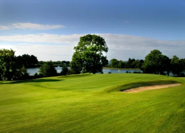 Scenic view of lush green golf course with lake backdrop.